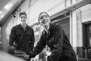 Female and male wearing overalls and safety glasses in a garage.